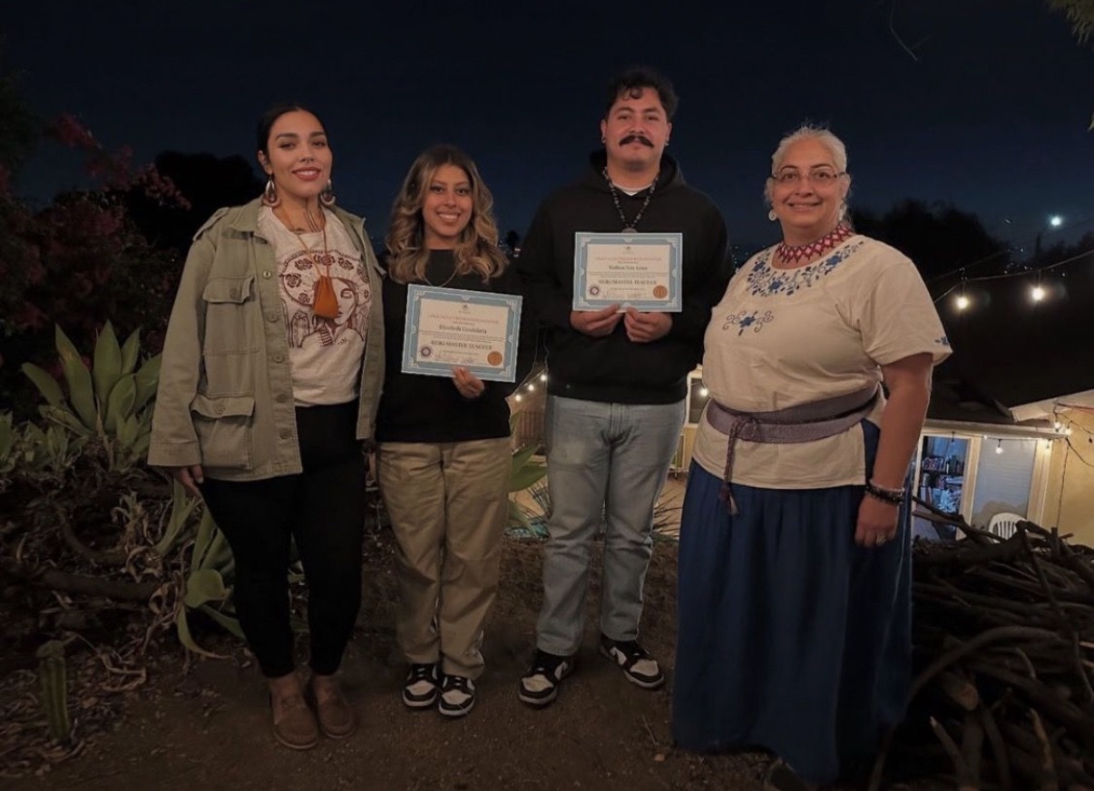 Ryanne standing with her maestra Sylvia as two students hold up their Holy Fire Reiki certificates at night