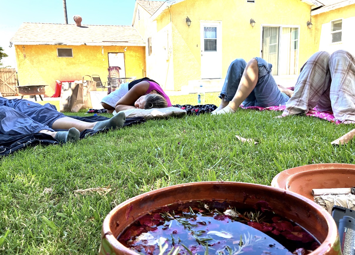 Participants resting on blankets in the grass beside clay bowls of flower water