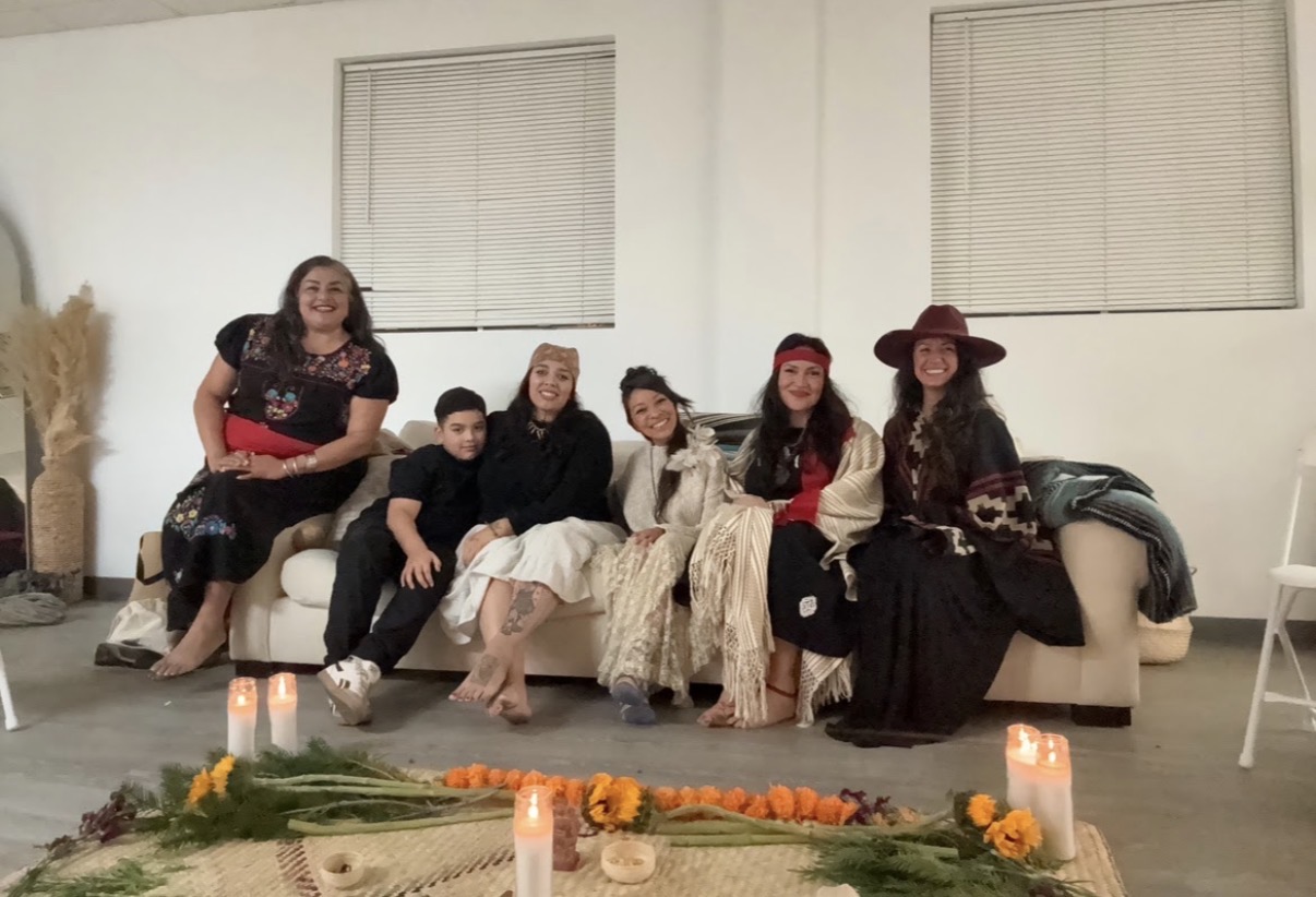 Ryanne and her son seated with Caminantes kin around a marigold and candle altar
