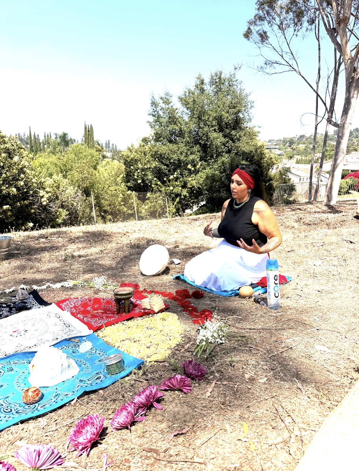 Ryanne with Caminantes, wearing a red bandana beside a flower altar on the land
