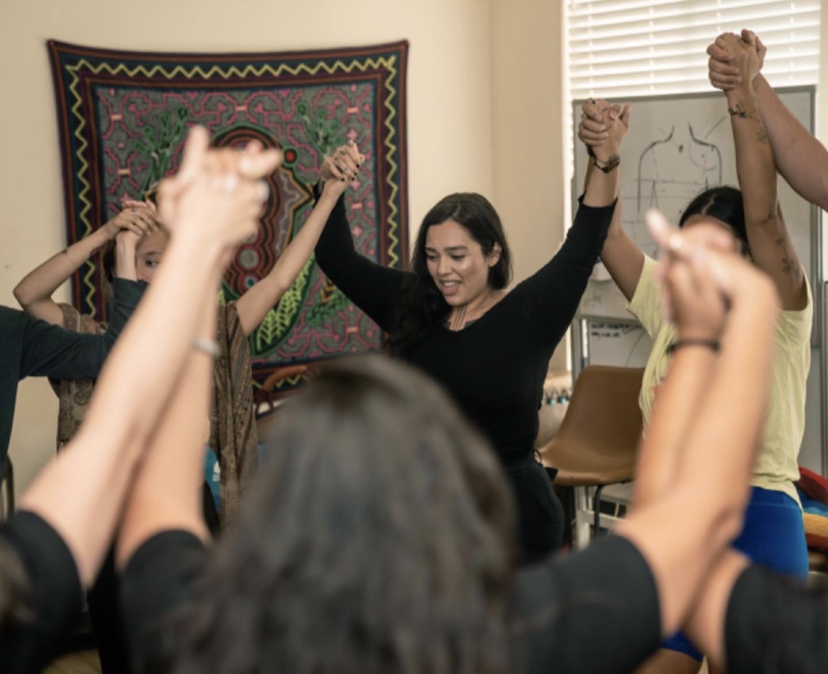 Ryanne at the center of a circle of women holding hands raised together during a teaching