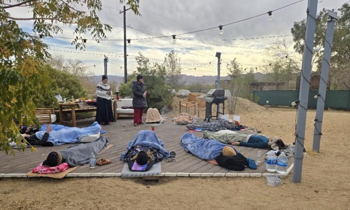 Participants resting under blankets on an outdoor deck in Joshua Tree as women tend the space