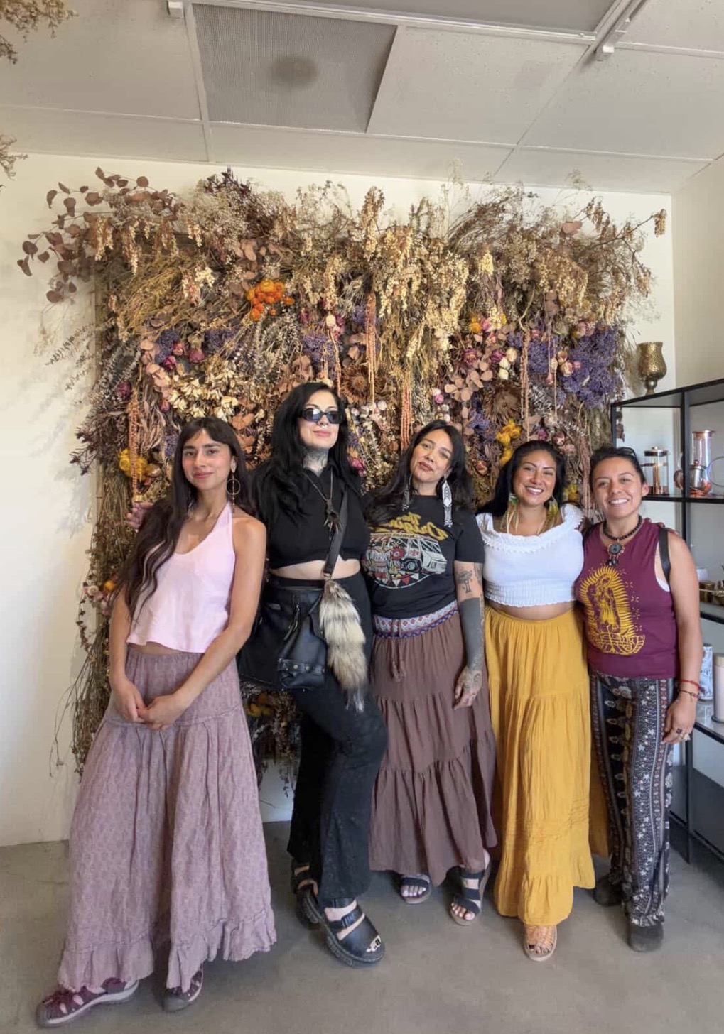 Five women standing together before a wall of dried flowers and herbs