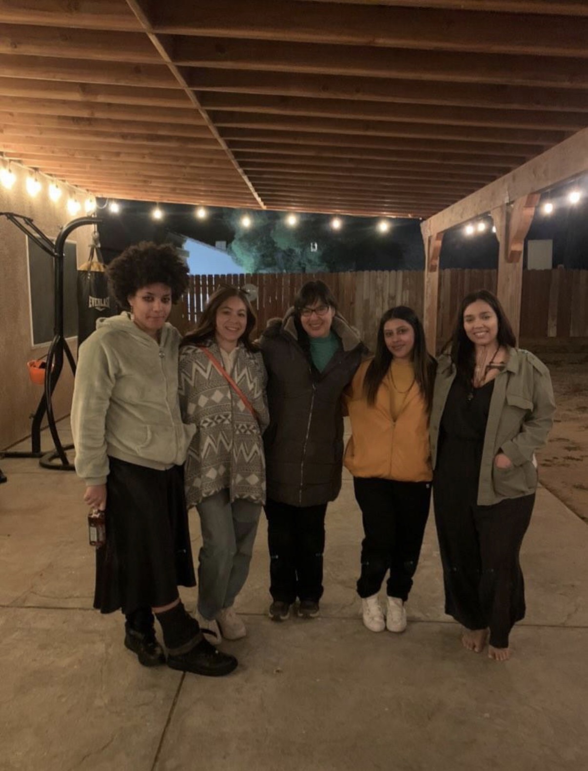 Ryanne and four women standing together under a patio strung with lights at dusk